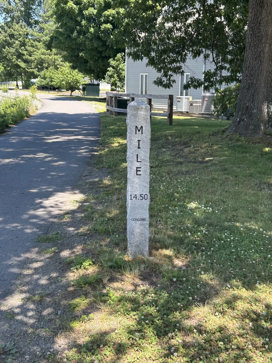 A granite mile marker beside a shaded walking path near the office