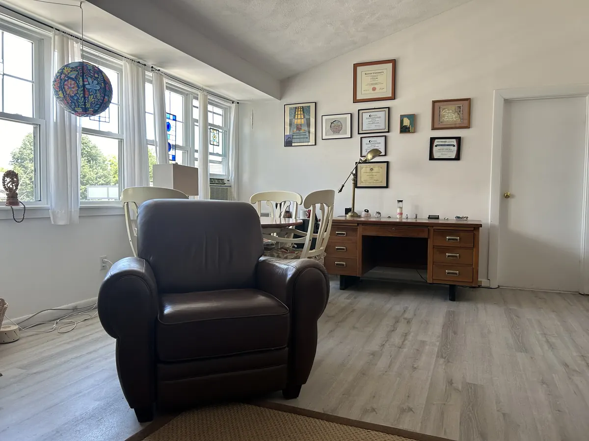 A bright room with a brown leather armchair, a wooden desk and framed diplomas
