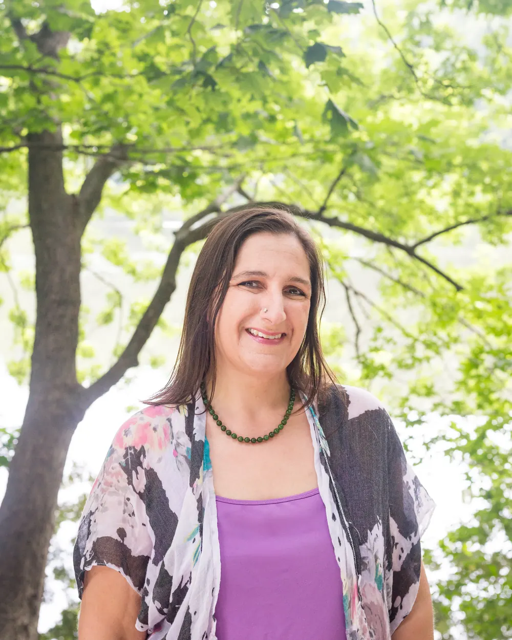Kara Katz outdoors under green trees, smiling
