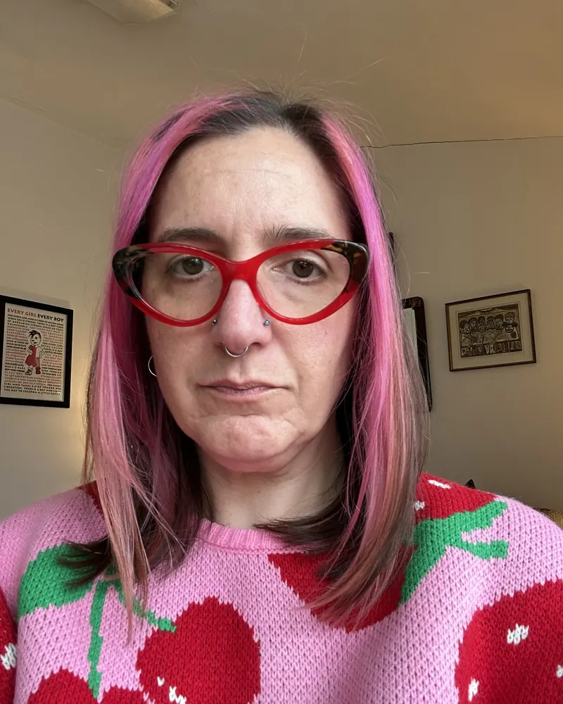 Kara Katz with bright pink hair and red cat-eye glasses